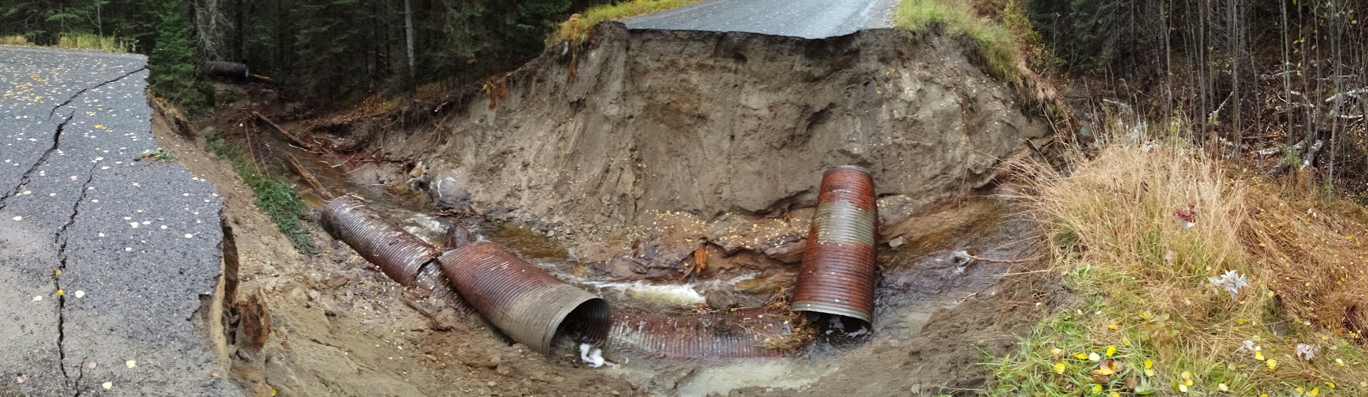 Road washed out down to the creek bed, with broken culvert sections in the water