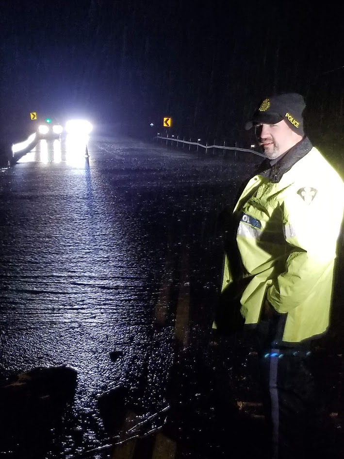OPP officer at a flooded road closure at night, with water flowing across the roadway