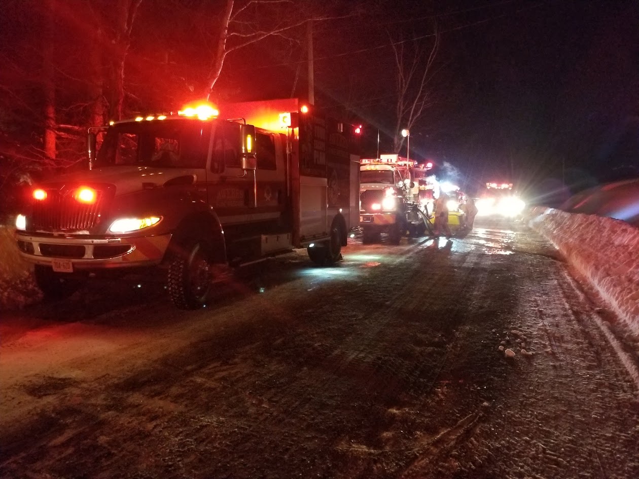 Several fire apparatus with emergency lights on a snowy road at night, crews working beside them