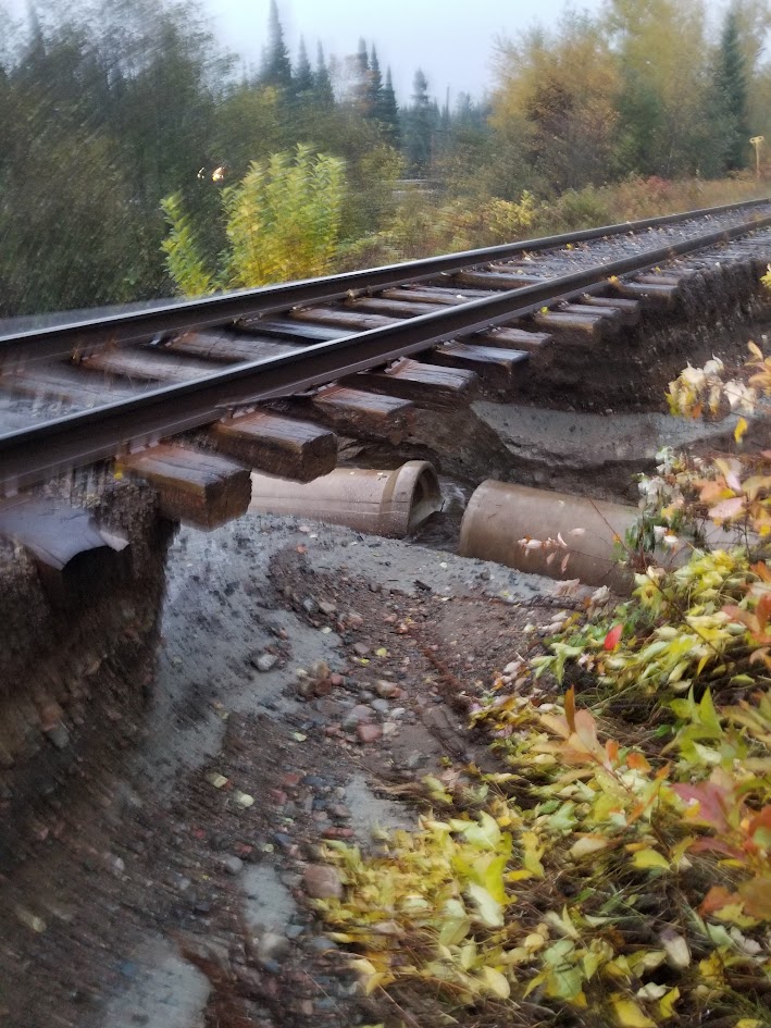 Railway track left hanging over a washout, ties unsupported and culvert pipes exposed beneath
