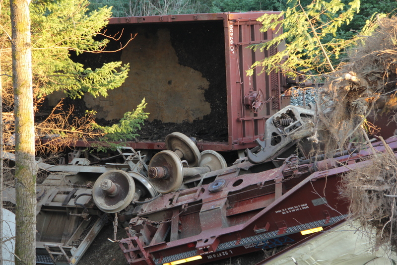 Overturned freight cars and wheel sets piled in the trees beside the track