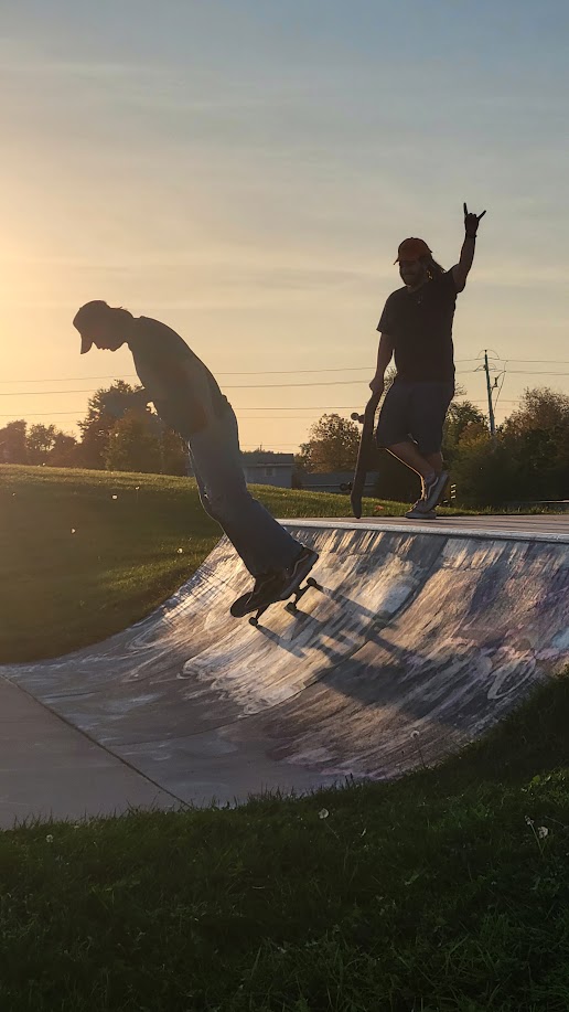 Two skateboarders silhouetted at sunset on the bowl of a free public skatepark